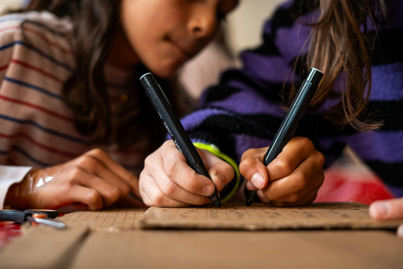 2 meisjes tekenen met zwarte stift op karton