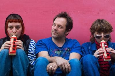 Johan Petit zittend tegen een roze muur geflankeerd door zijn muzikanten met elk een melodica