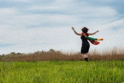 dame in zwarte korte jurk in een veld met wapperende lange kleurige sjaal