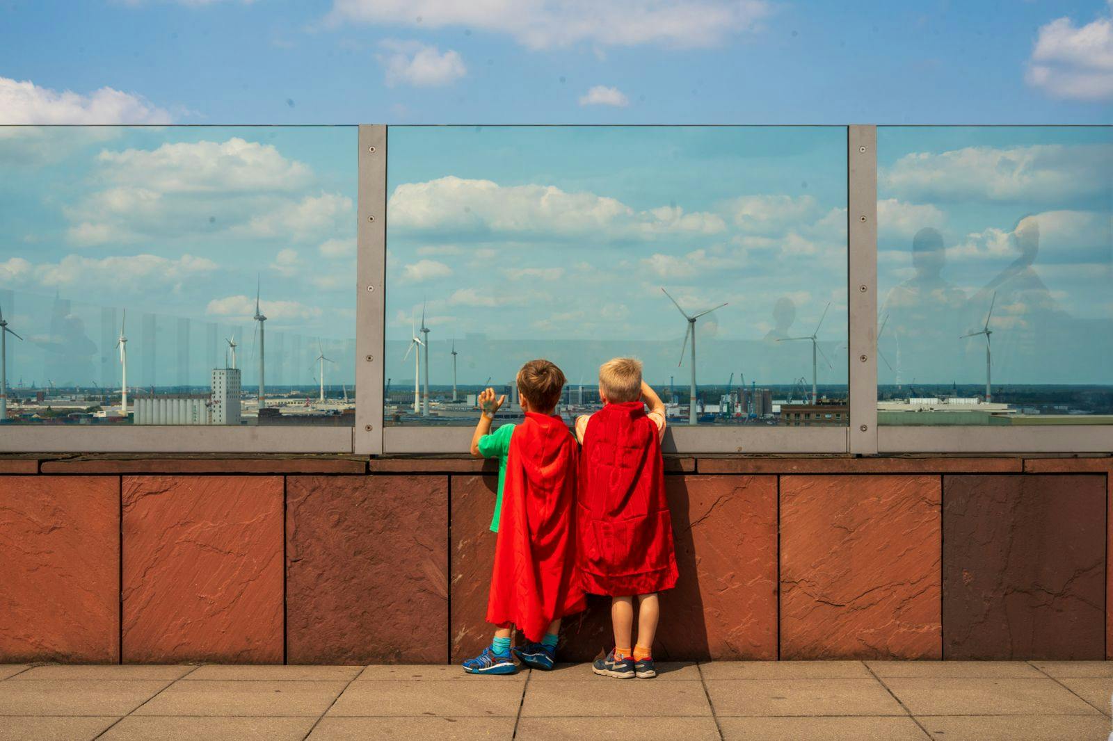 Twee kindjes met een cape kijken naar de skyline van antwerpen op het dak van het mas